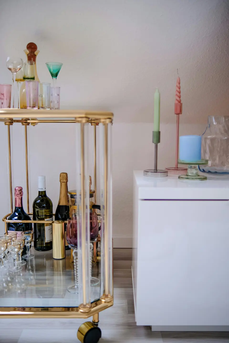 A brass and glass two-tier bar cart styled with bottles and glassware in a bright room