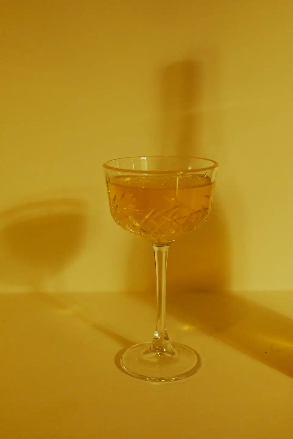 An etched crystal coupe holding an amber cocktail against a warm golden backdrop